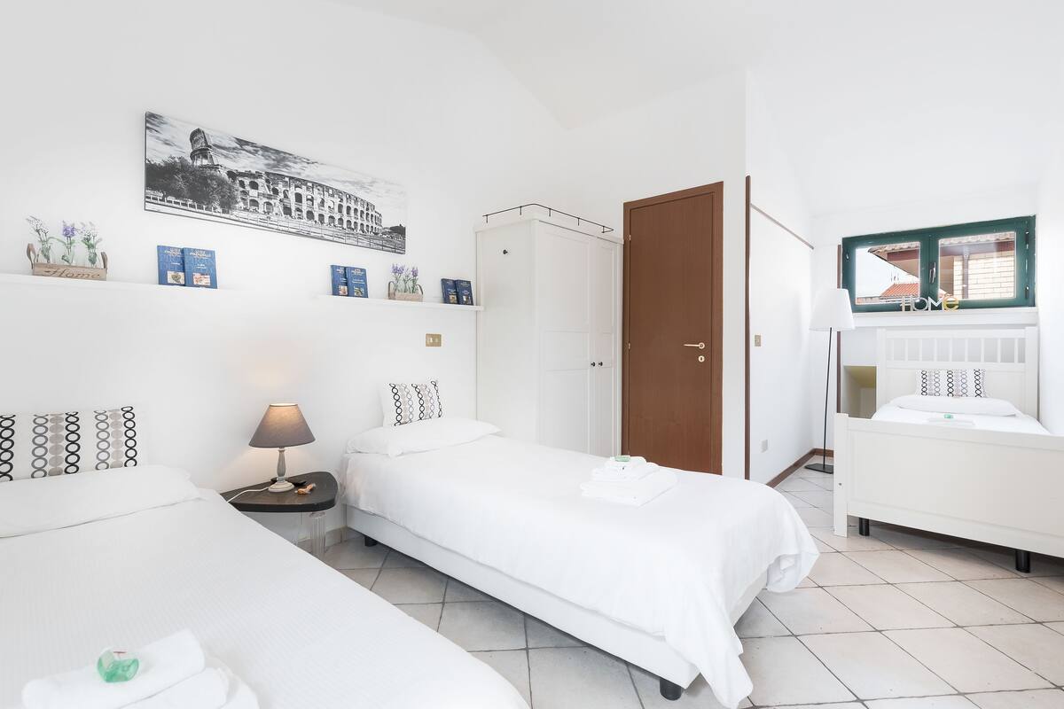 A hotel room with two single beds, a wardrobe, a desk with a lamp, and a window with a view.