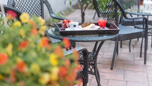 Ein Essbereich im Freien mit Korbstühlen und einem Tisch, auf dem eine Speiseplatte mit Erdbeeren und einem Glas roter Saft steht.