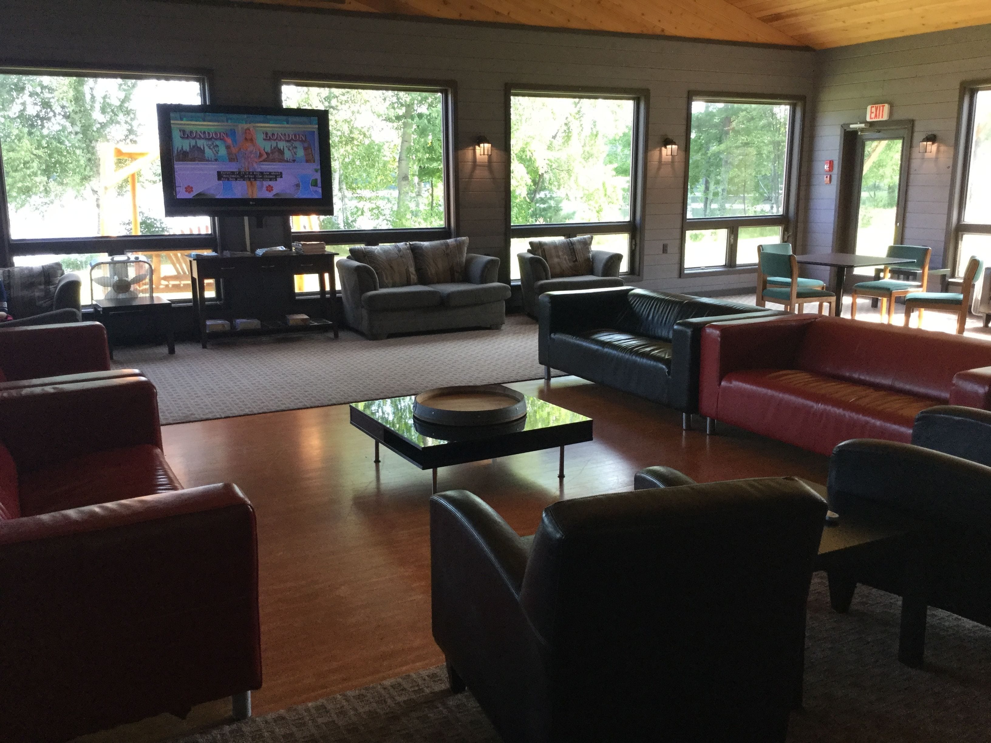 A spacious living room with multiple seating areas, a flat-screen TV, and large windows offering a view of trees.