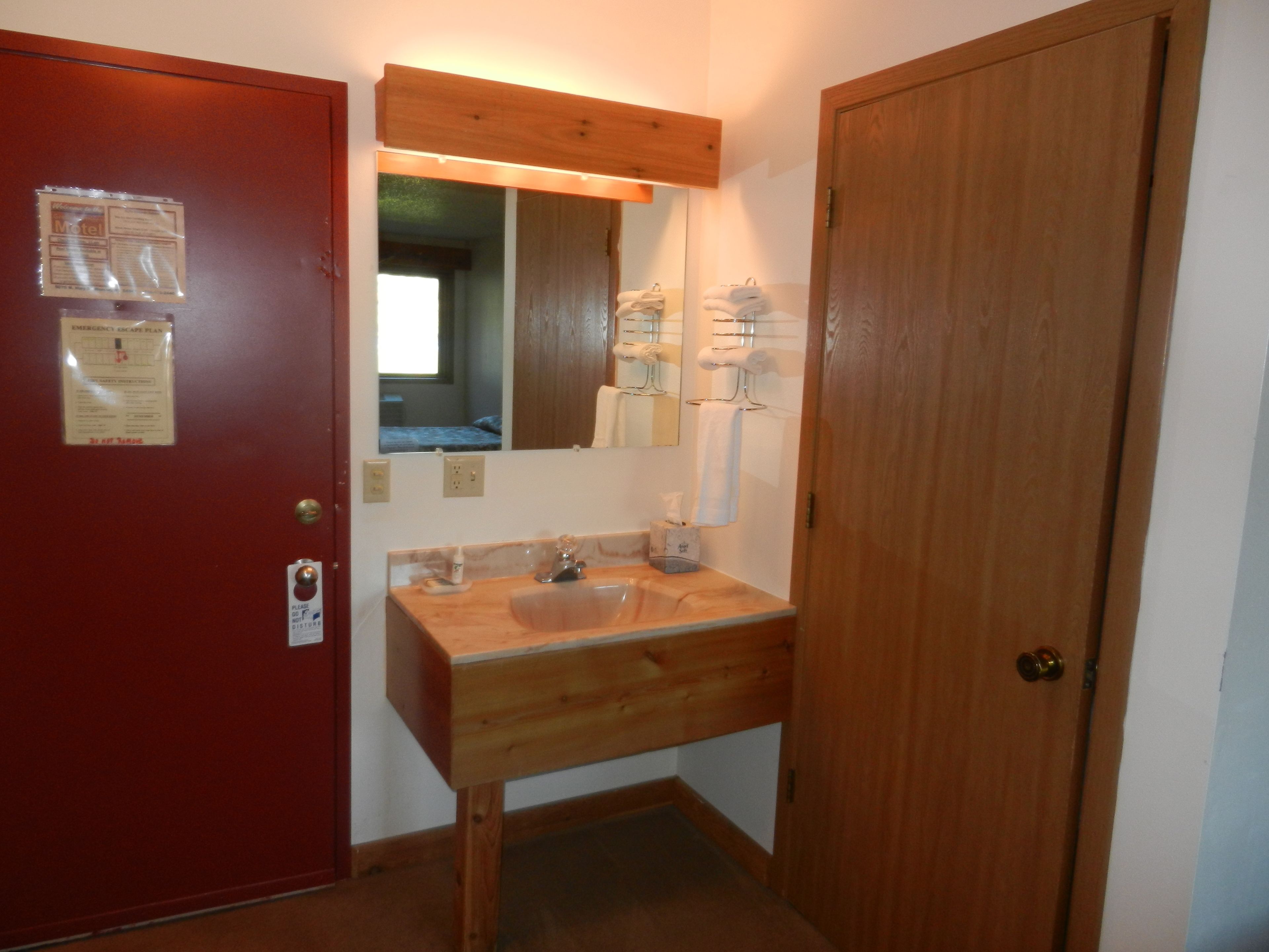 A bathroom with a wooden vanity, a sink, a mirror, and a door.