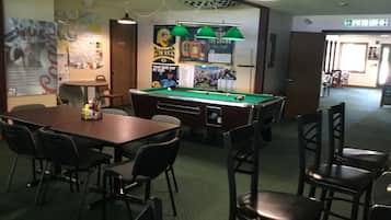Une table de billard dans une pièce entourée de chaises, une table avec des bouteilles et des affiches accrochées au mur.