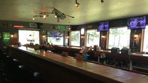 A bar area with a long counter, bar stools, and a television screen displaying sports.