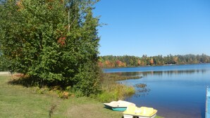 A calm lake with boats on the shore, surrounded by trees and a clear sky.