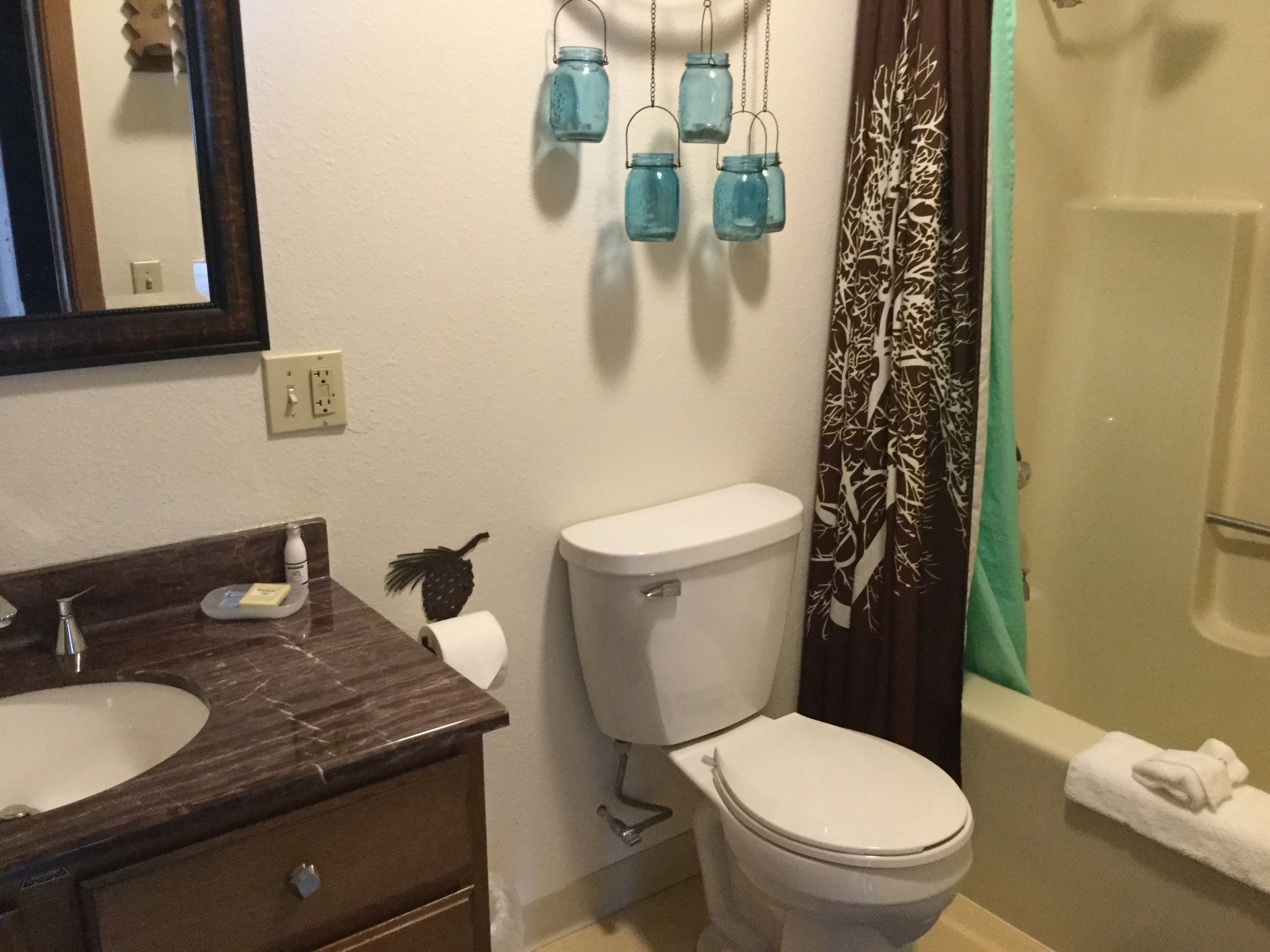 Ein Badezimmer mit Marmorwaschbecken, Toilette und einer Duschvorhang mit Blättermotiv.