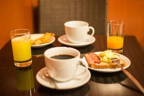 A breakfast setting with a glass of orange juice, two cups of coffee, toast with eggs, and a glass of orange juice on a table. - Tecte Guest House (Cusco)