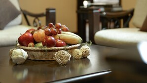 Uma cesta de vime com frutas sobre uma mesa de madeira escura em um quarto com um sofá e um espelho.