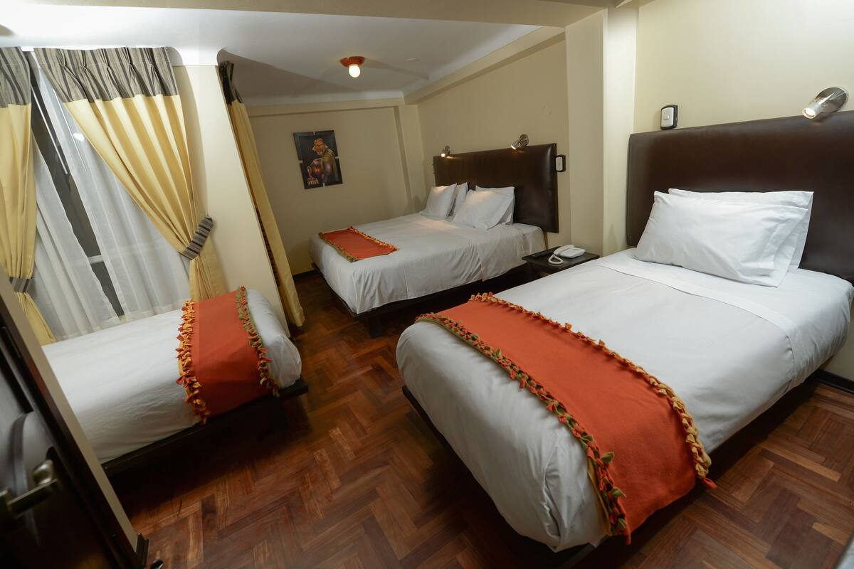 Une chambre d’hôtel avec deux lits simples, un plancher en bois, une table de chevet avec un téléphone et une lampe fixée au mur.