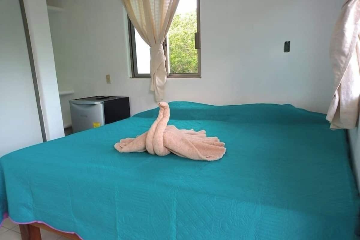 A room with a bed covered in a teal bedspread and a towel arranged in a swan shape.