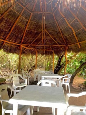 Un área de estar al aire libre con mesas y sillas bajo una estructura de techo de paja.