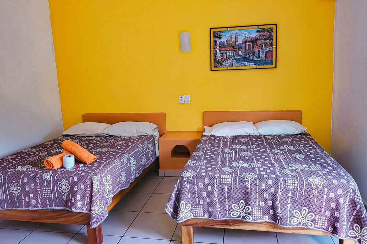 A room with two beds, each with a patterned bedspread, a small nightstand, and a wall-mounted air conditioning unit.
