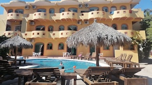 Un hotel con piscina, sillones de madera y sombrillas de paja.