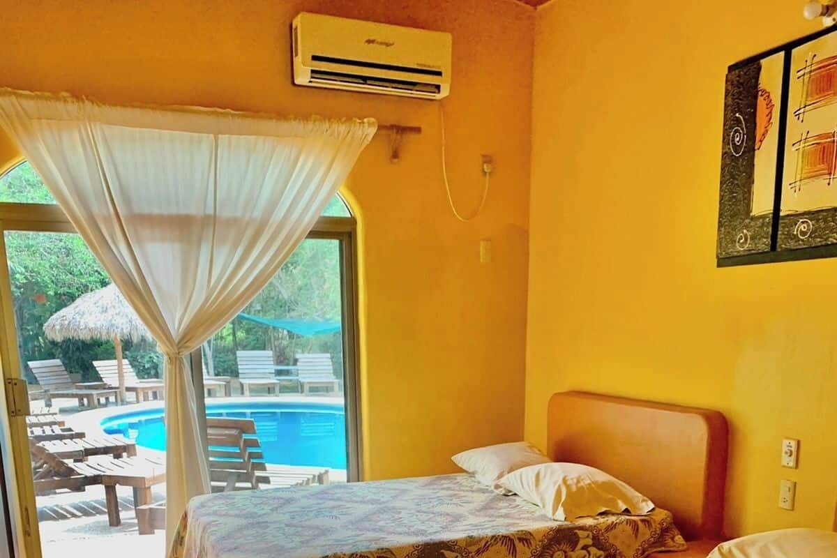 A room with two beds, a window with a view of a pool, and an air conditioning unit.