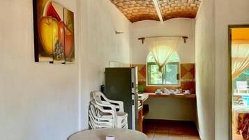 A room with a dining table and chairs, a kitchen area with a window, and a brick ceiling.
