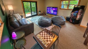A living room with a sofa, a coffee table, a chess table, a TV, and a gaming console. - Brittany Motel (Manchester Center)