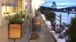 A building with a covered outdoor area, wooden benches, and potted plants. - Brittany Motel (Manchester Center)