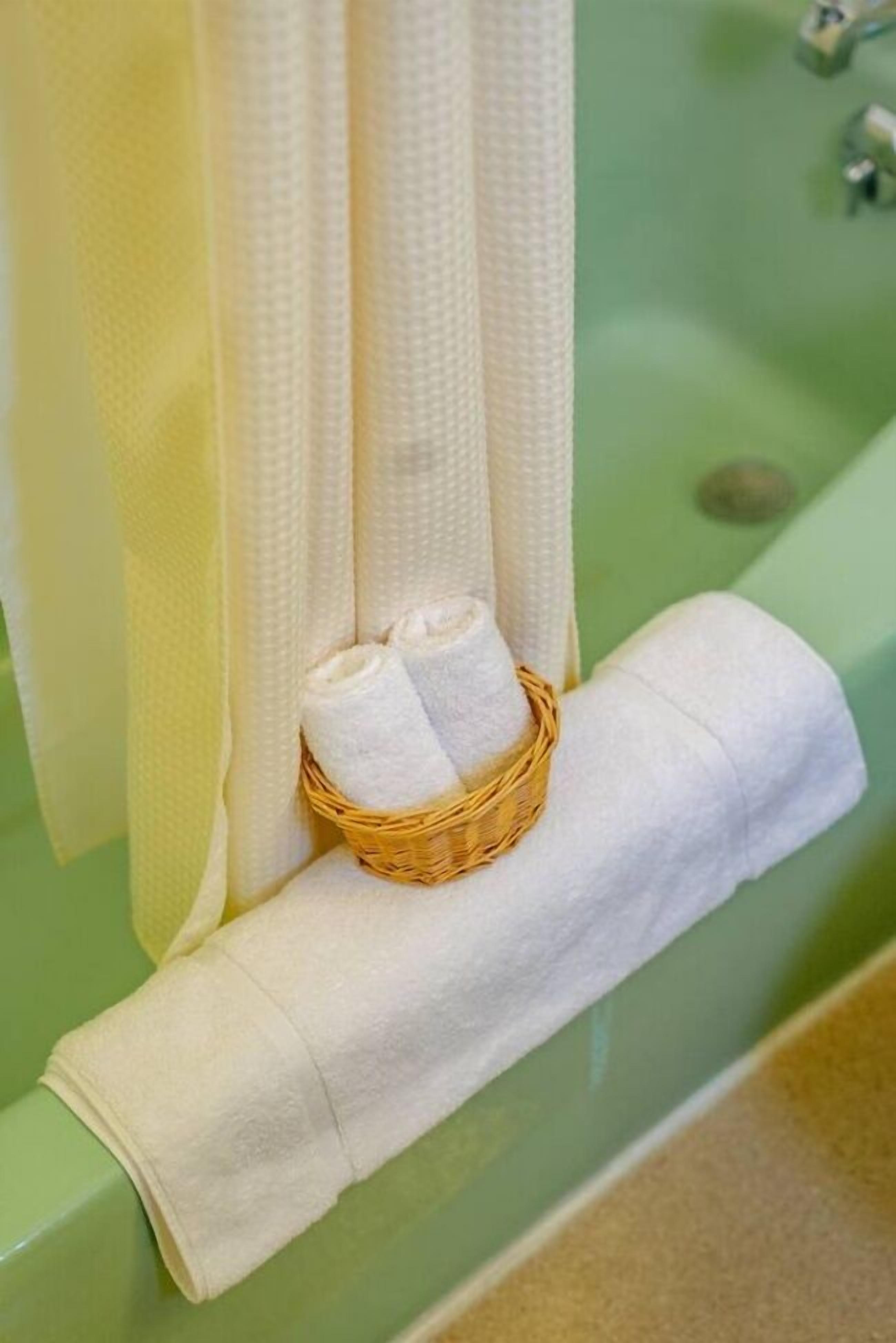 A bathroom with a green bathtub, a white towel, and a wicker basket with two rolled-up towels.