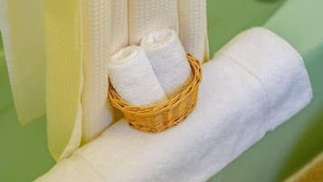 A bathroom with a green bathtub, a white towel, and a wicker basket with two rolled-up towels.
