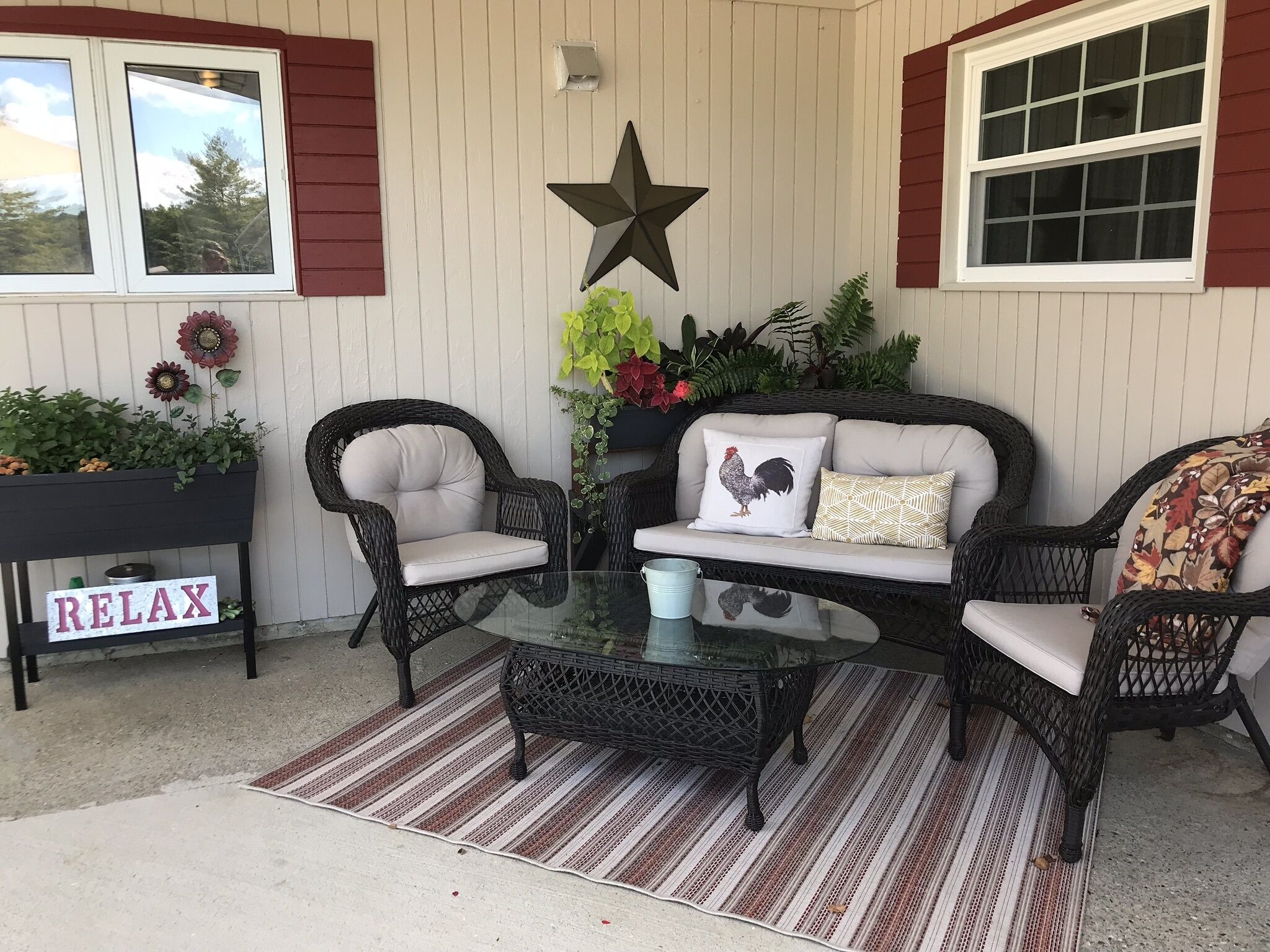 Un patio con mobiliario de mimbre, una mesa de vidrio y un letrero que dice 'RELAX'.