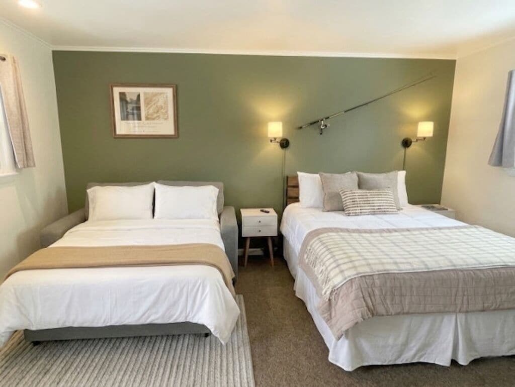 A hotel room with two beds, a nightstand, a framed picture on the wall, and two wall-mounted lamps.