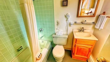 A bathroom with a green tiled wall, a white toilet, a bathtub, and a wooden vanity with a sink.