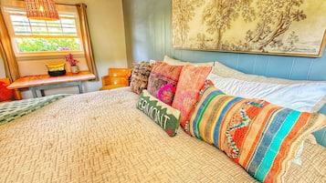 Une chambre avec un grand lit, des coussins colorés, un luminaire suspendu, une fenêtre donnant sur un beau paysage et un tableau au mur.