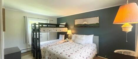 Un dormitorio con una cama litera, una mesita de noche con lámpara y una obra de arte colgada en la pared.