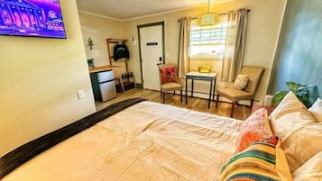 Een hotelkamer met een bed, een bureau, een stoel, een kleine tafel, een televisie en een raam met gordijnen.