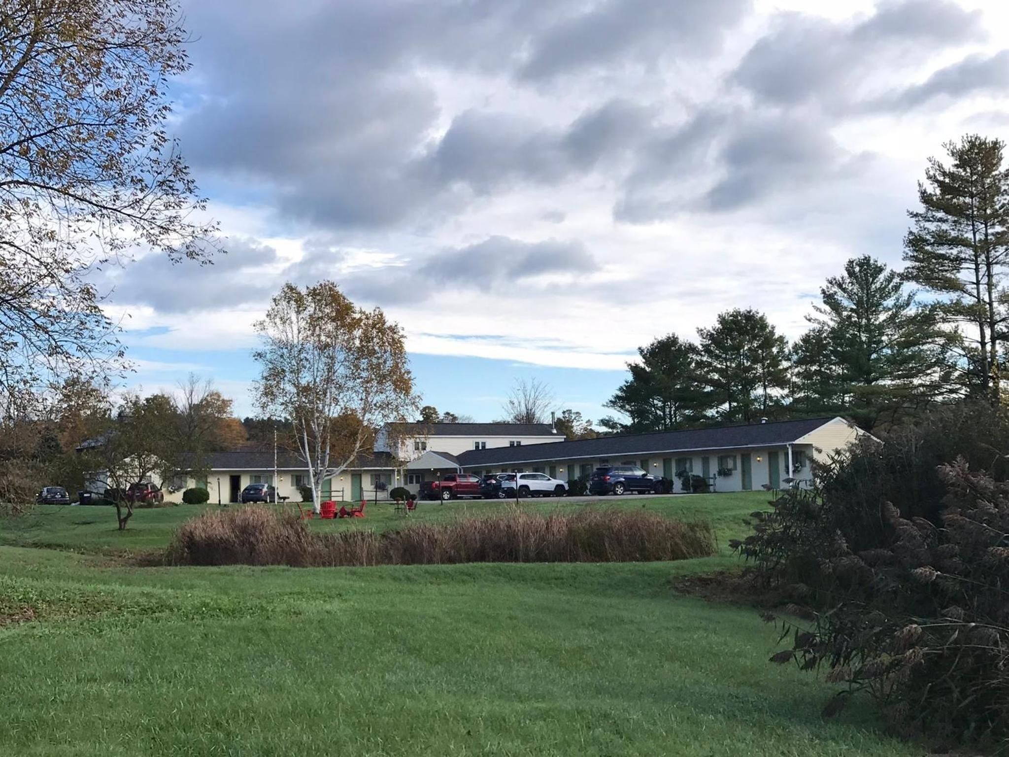 A motel with a parking lot, several cars, and a grassy area with trees.
