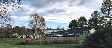A motel with a parking lot, several cars, and a grassy area with trees.
