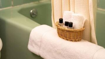 A bathroom with a green tiled wall, a bathtub, a white towel, and a wicker basket with toiletries.