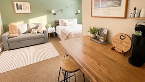 A cozy room with a sofa, a bed, a wooden table, and a coffee machine. - Brittany Motel (Manchester Center)