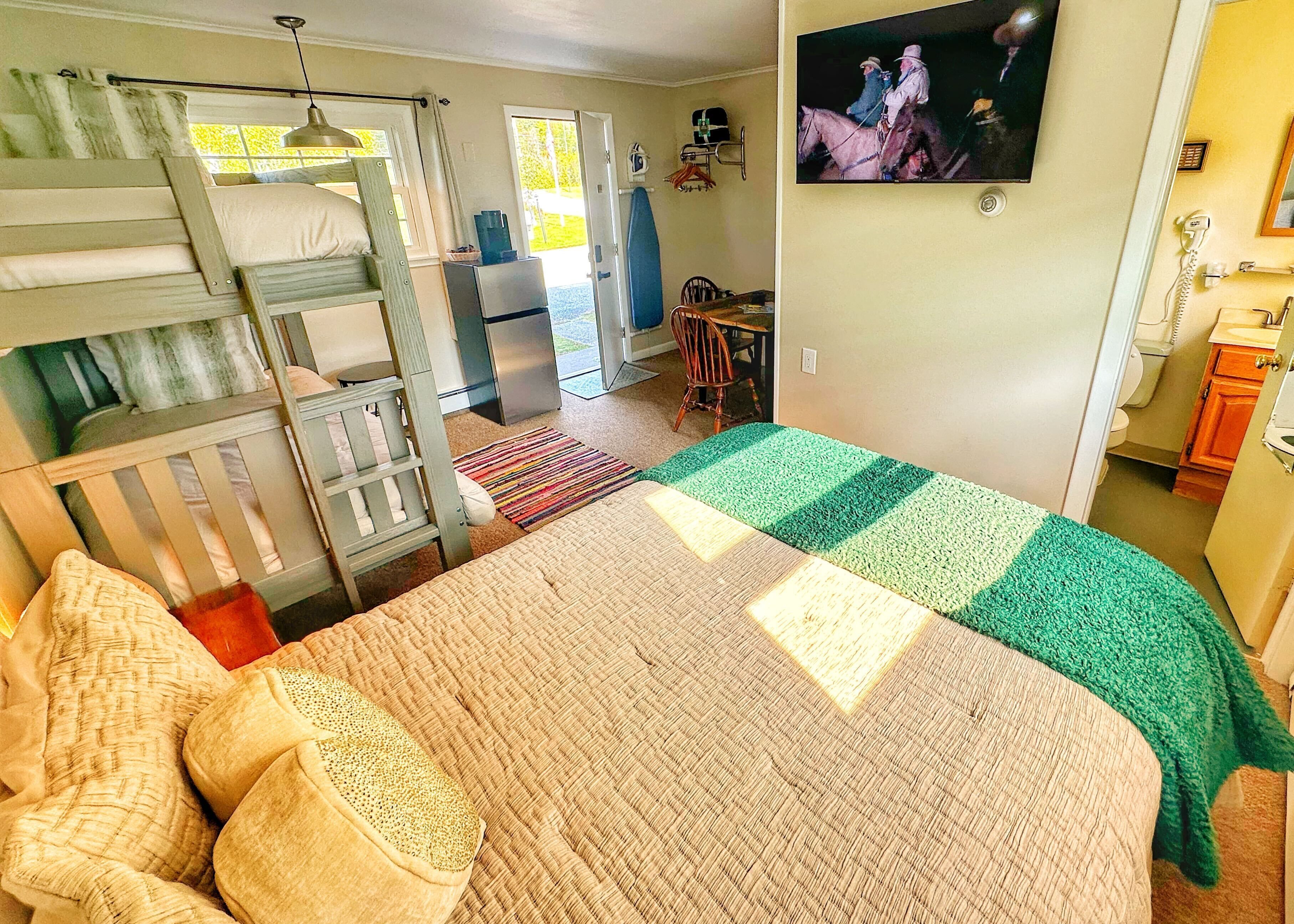 A bedroom with bunk beds, a desk, and a television on the wall.