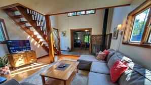 A spacious living room with a wooden staircase, a television, a sofa set, and a fireplace. - Brittany Motel (Manchester Center)