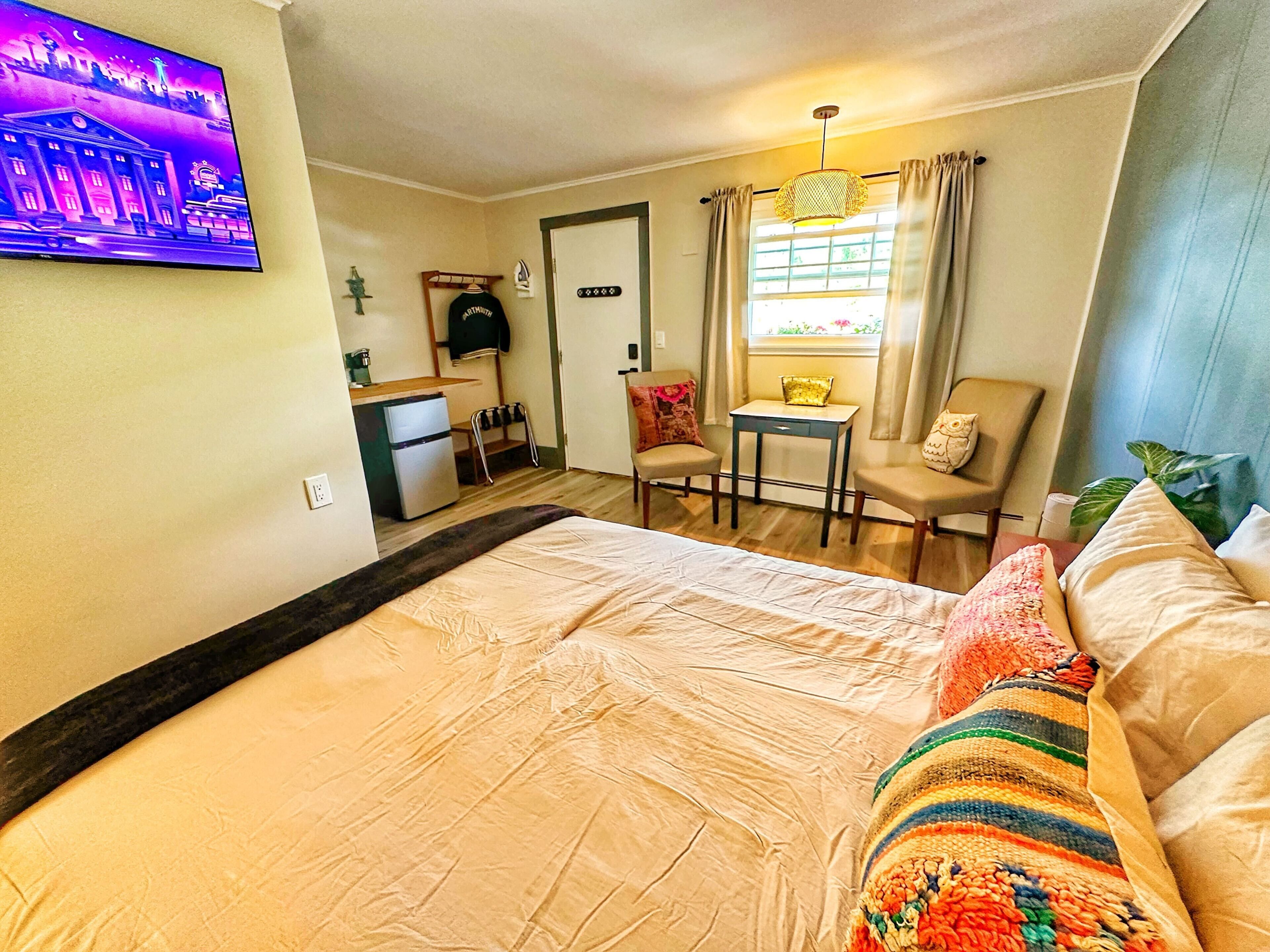 Habitación de hotel con cama, un escritorio pequeño, una silla, televisión y ventana con cortinas.