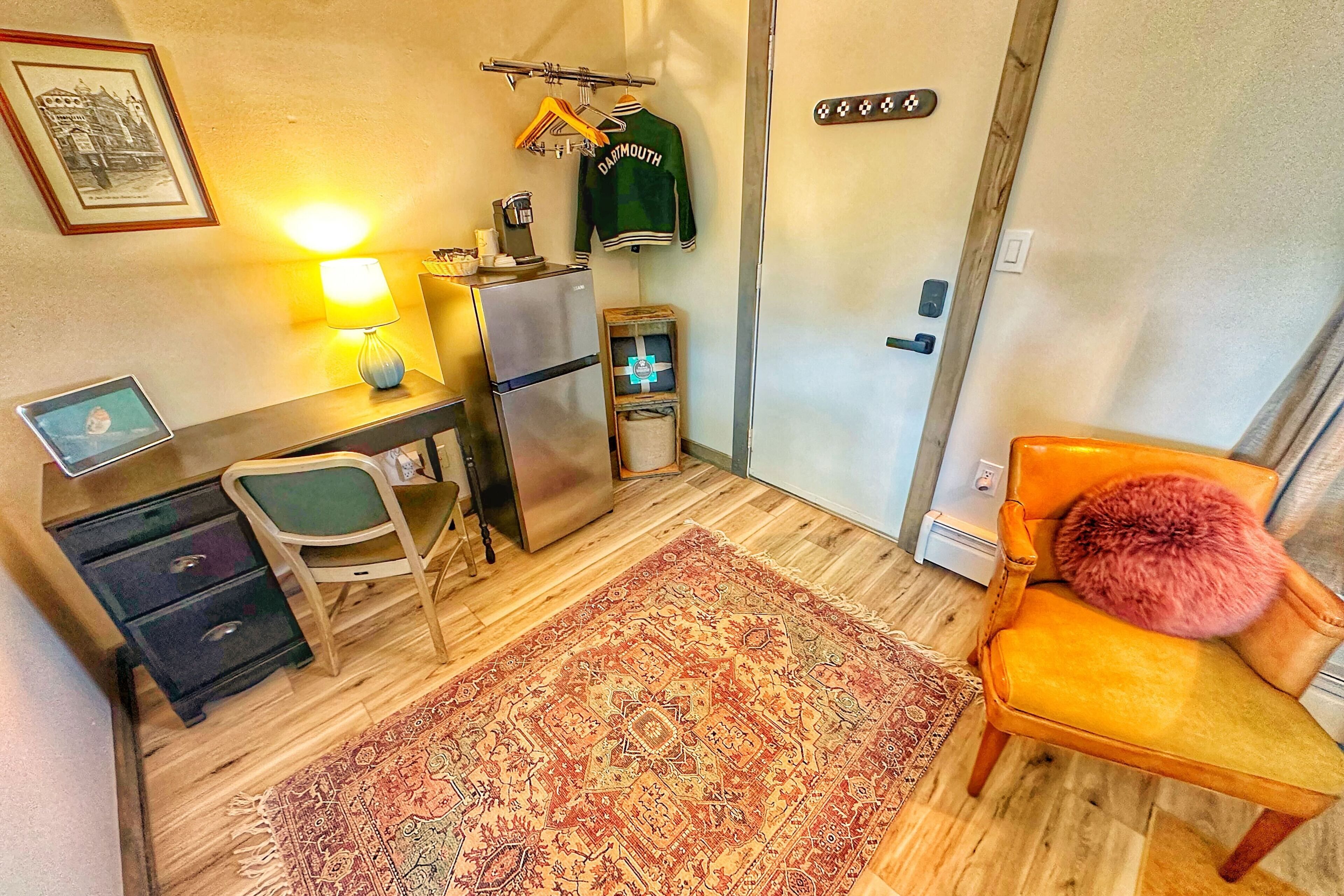 A compact living space with a desk, chair, refrigerator, and a cozy rug.