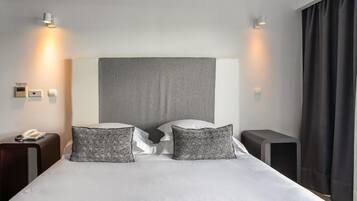 Una habitación de hotel con una cama grande, dos mesitas de noche, un teléfono y una cortina oscura.