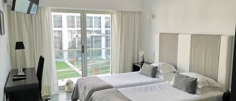 Habitación de hotel con dos camas, un escritorio, una silla, un televisor montado en la pared y vistas al exterior a través de un gran ventanal.