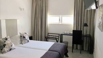 Habitación de hotel con dos camas, un escritorio, una silla y un televisor.