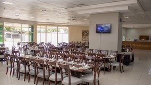 Une grande salle de conférence équipée de plusieurs tables et chaises, d’un téléviseur fixé au mur et d’un comptoir d’accueil.
