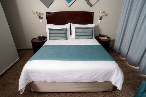 Une chambre d’hôtel avec un grand lit, deux tables de chevet, une petite table et une tête de lit.