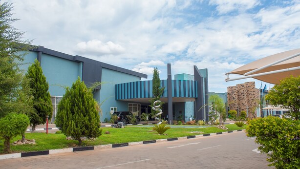 Un bâtiment moderne à la façade bleue, doté d’un espace de stationnement et d’un jardin aménagé avec des arbres et des arbustes.