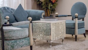 Un salon moderne avec un canapé bleu, un fauteuil assorti et un fauteuil à motifs. Une petite table d’appoint décorative, avec un plateau en verre, est placée entre les fauteuils.