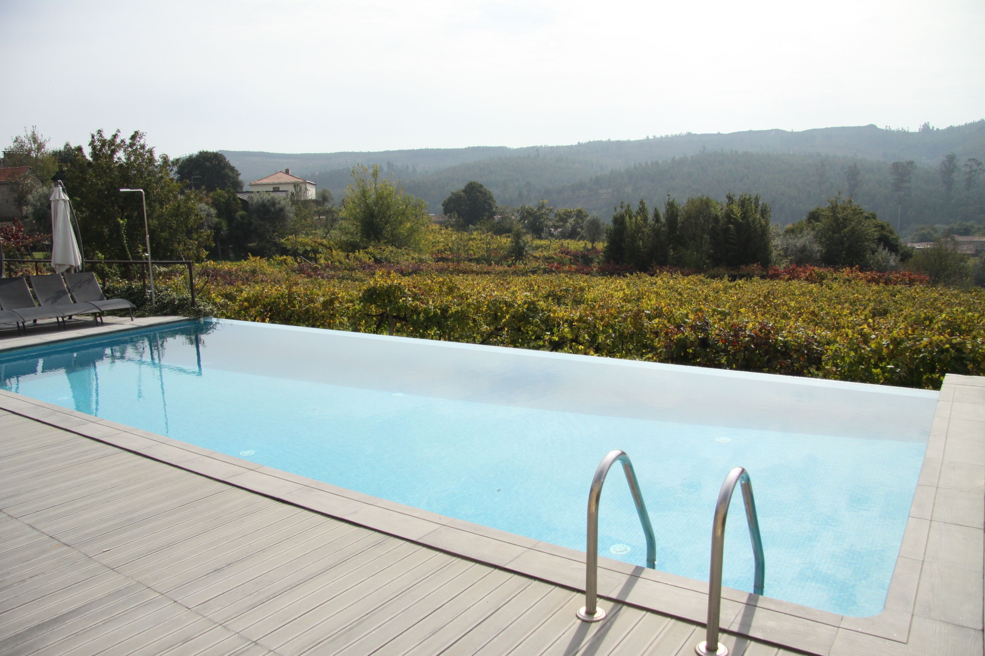 Una piscina amb terrassa de fusta, gandules i vistes al paisatge circumdant.