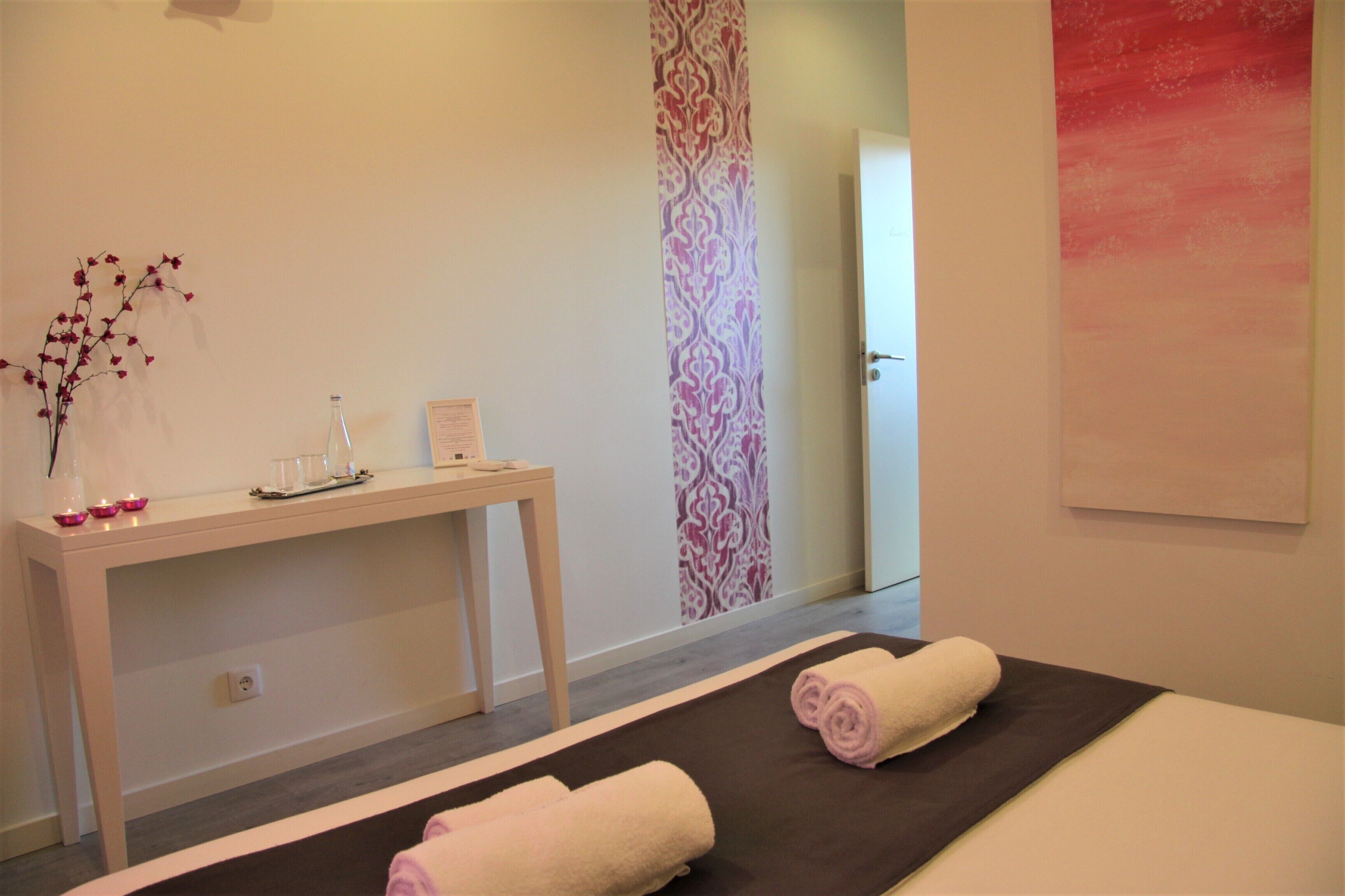A spa room with a massage table, towels, a small table with candles, and a decorative wall panel.