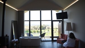 Een moderne badkamer met een groot bad, een spiegel en een raam met uitzicht op het groen.