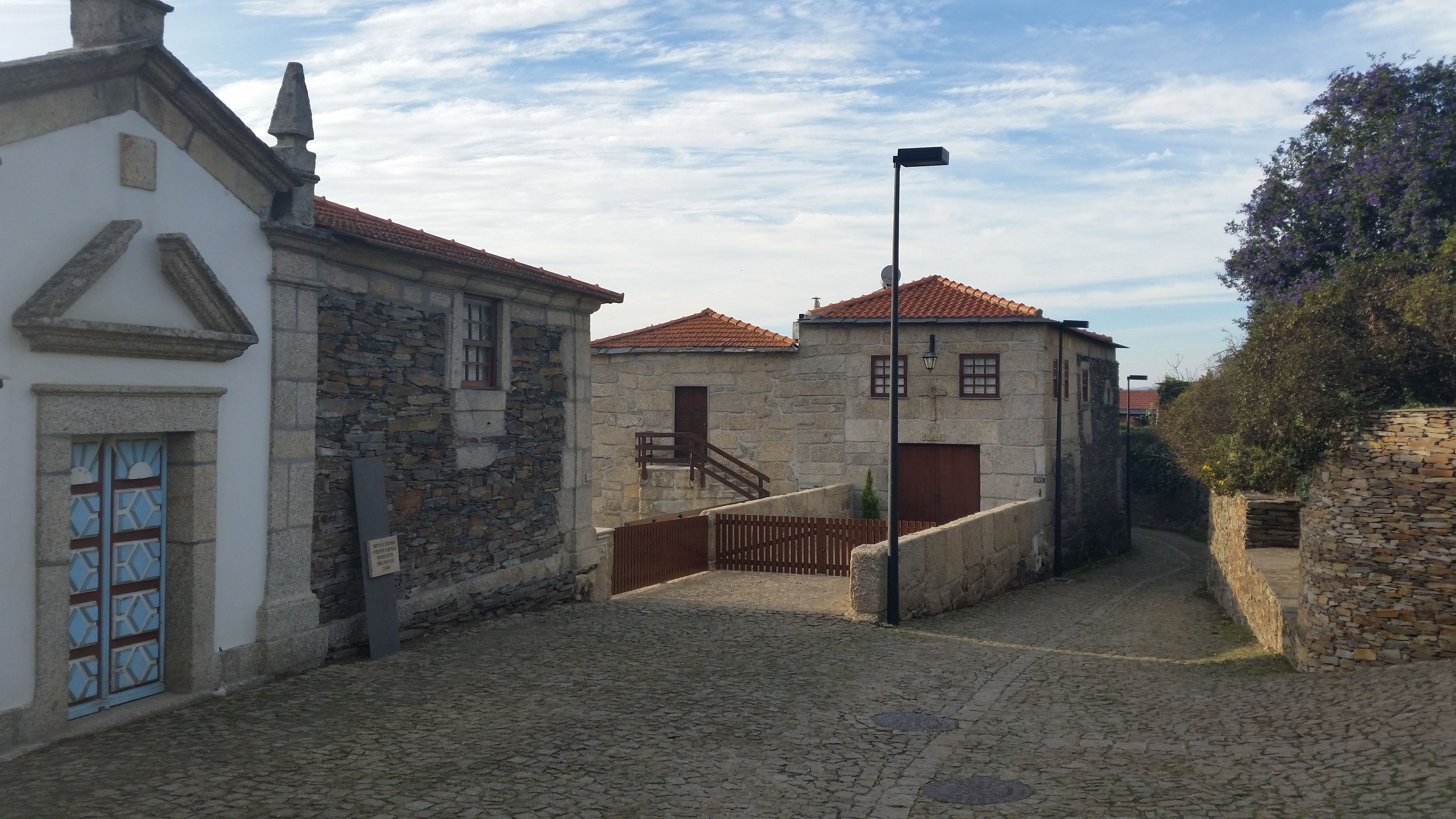 A cobblestone street with stone buildings, a wooden gate, and a street lamp.