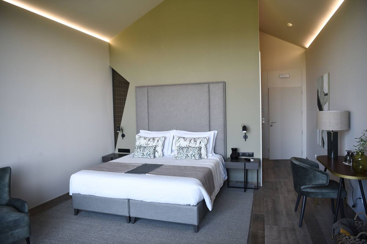 Ein modernes Hotelzimmer mit einem großen Bett, Nachttischen, einem Schreibtisch und einem Sessel.