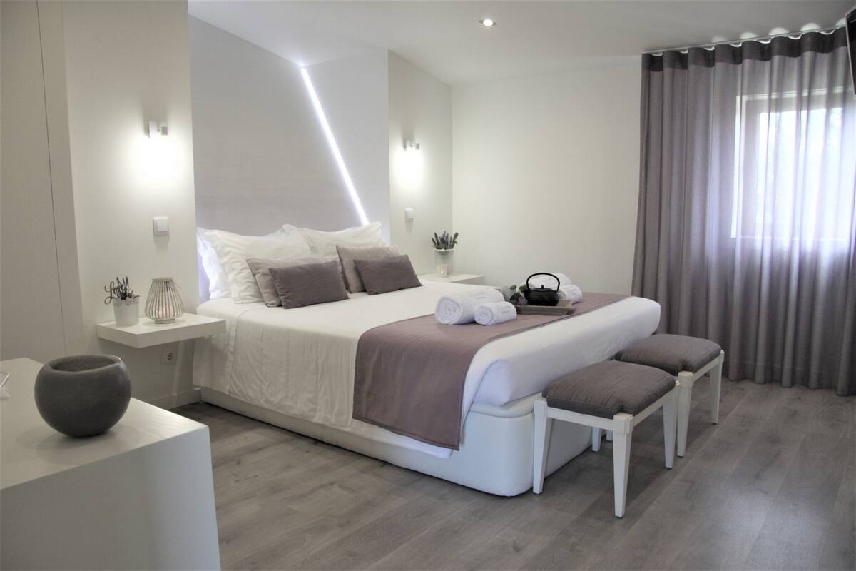 Ein modernes Schlafzimmer mit einem großen Bett, Nachttischen, einer Bank und einer Vase.