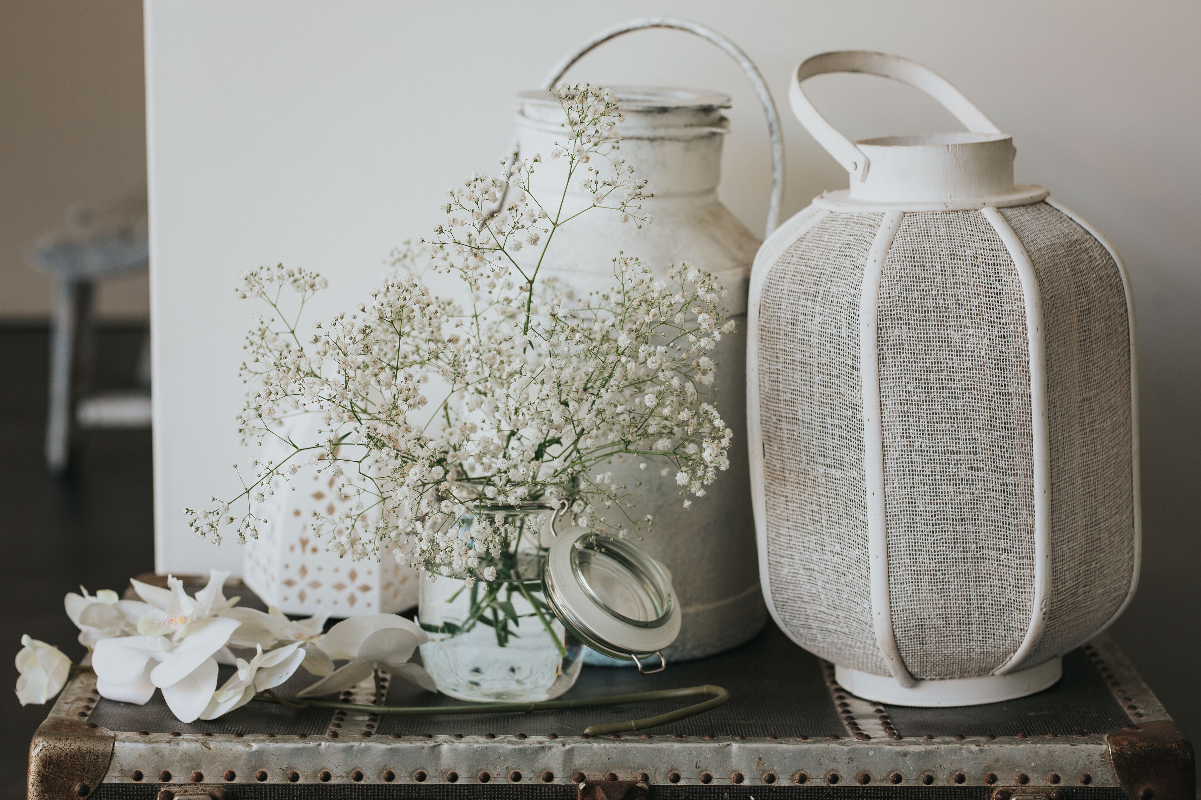 A rustic table with a vintage lantern, a metal milk jug, and a glass vase with white flowers.
