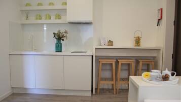 A modern kitchen with white cabinets, a white countertop, a sink, and a vase with flowers. There are two wooden stools and a tray with a teapot and cups.